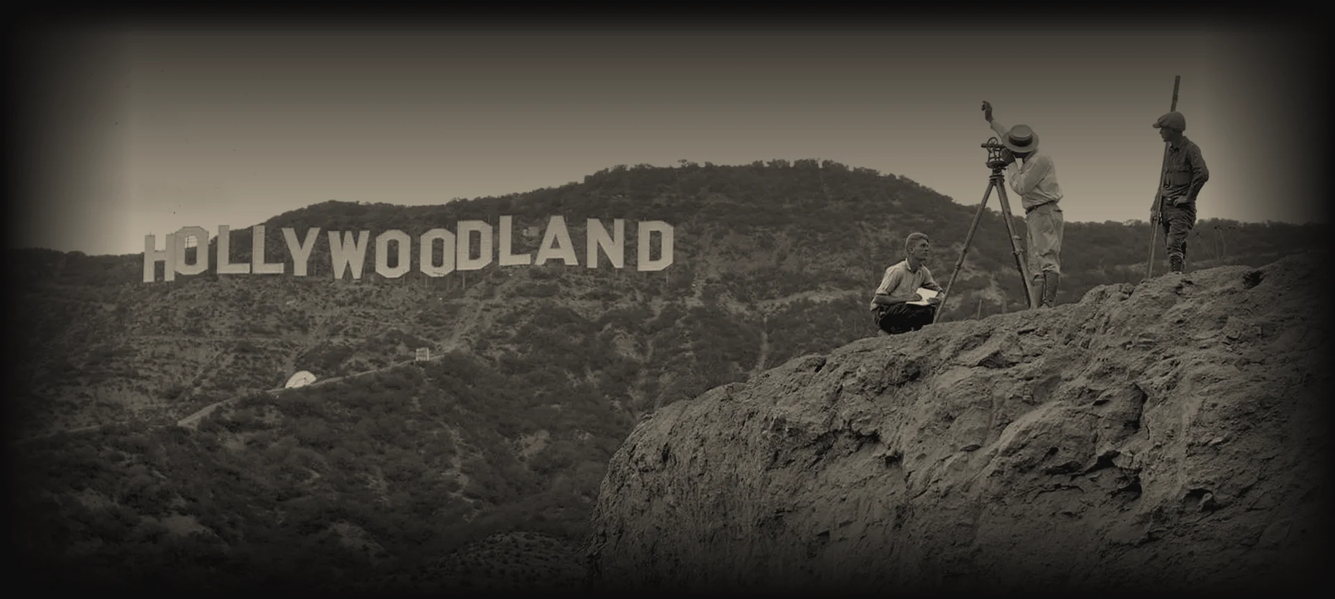 Historic 1920s photograph of the Hollywoodland sign on the Hollywood Hills, with three surveyors in the foreground