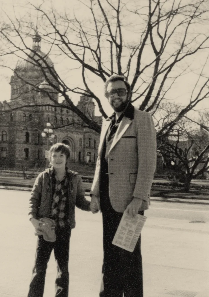 Black and white photograph of Jim Meier as a boy holding hands with his father, John Meier, in front of the British Columbia Parliament Buildings